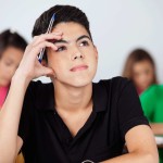 Thoughtful teenage boy looking up while sitting in classroom