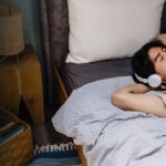 Student lying in bed listening to music on earphones