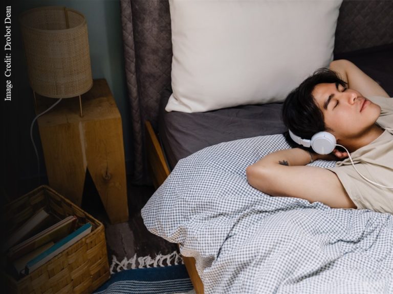 Student lying in bed listening to music on earphones