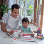 portrait of father teaching daughter how to read by using simple words and letters on a flash card at home