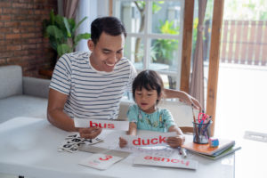 portrait of father teaching daughter how to read by using simple words and letters on a flash card at home