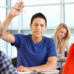 Hispanic student wearing a blue shirt raising his hand to ask a question in class