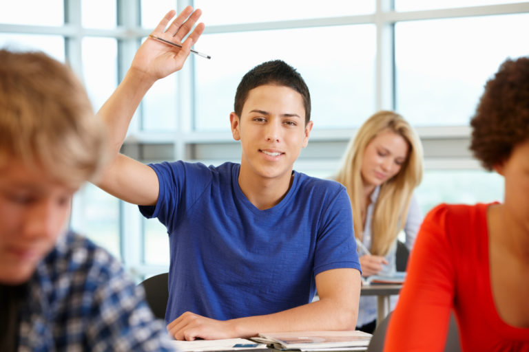 Hispanic student wearing a blue shirt raising his hand to ask a question in class