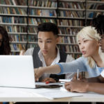 4 students sitting at a table discussing something visible on a laptop