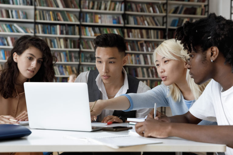 4 students sitting at a table discussing something visible on a laptop