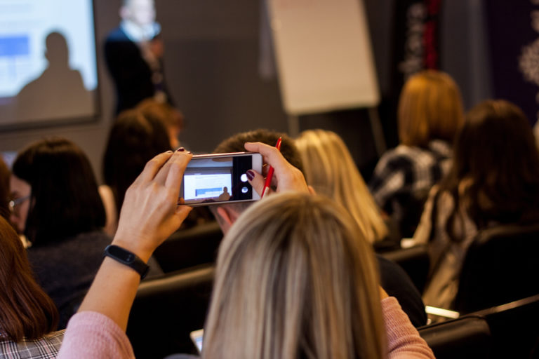 Woman holding up mobile phono to take photo of speaker and slides