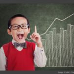 Child wearing a bow tie and a happy expression standing in front of a chalkboard with a bar graph showing steady increases