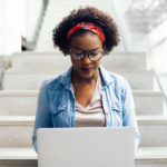 Young woman sitting on a brightly lit staircase working on a computer