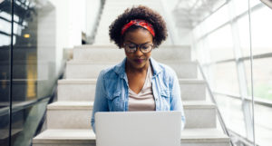 Young woman sitting on a brightly lit staircase working on a computer