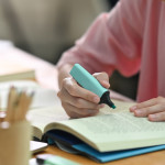 Female student using pale blue highlighter in a book