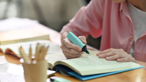 Female student using pale blue highlighter in a book