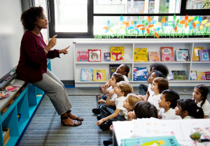 Kindergarten students sitting on the floor, listening to the teacher at the chalkboard