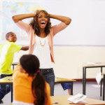 Exasperated teacher standing in the middle of a chaotic classroom, holding her hands on her head and shouting