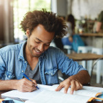 College student smiling while taking notes on while studying