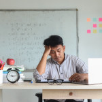 Stressed teacher sitting in front of a white board with comlex mathematical equations on it