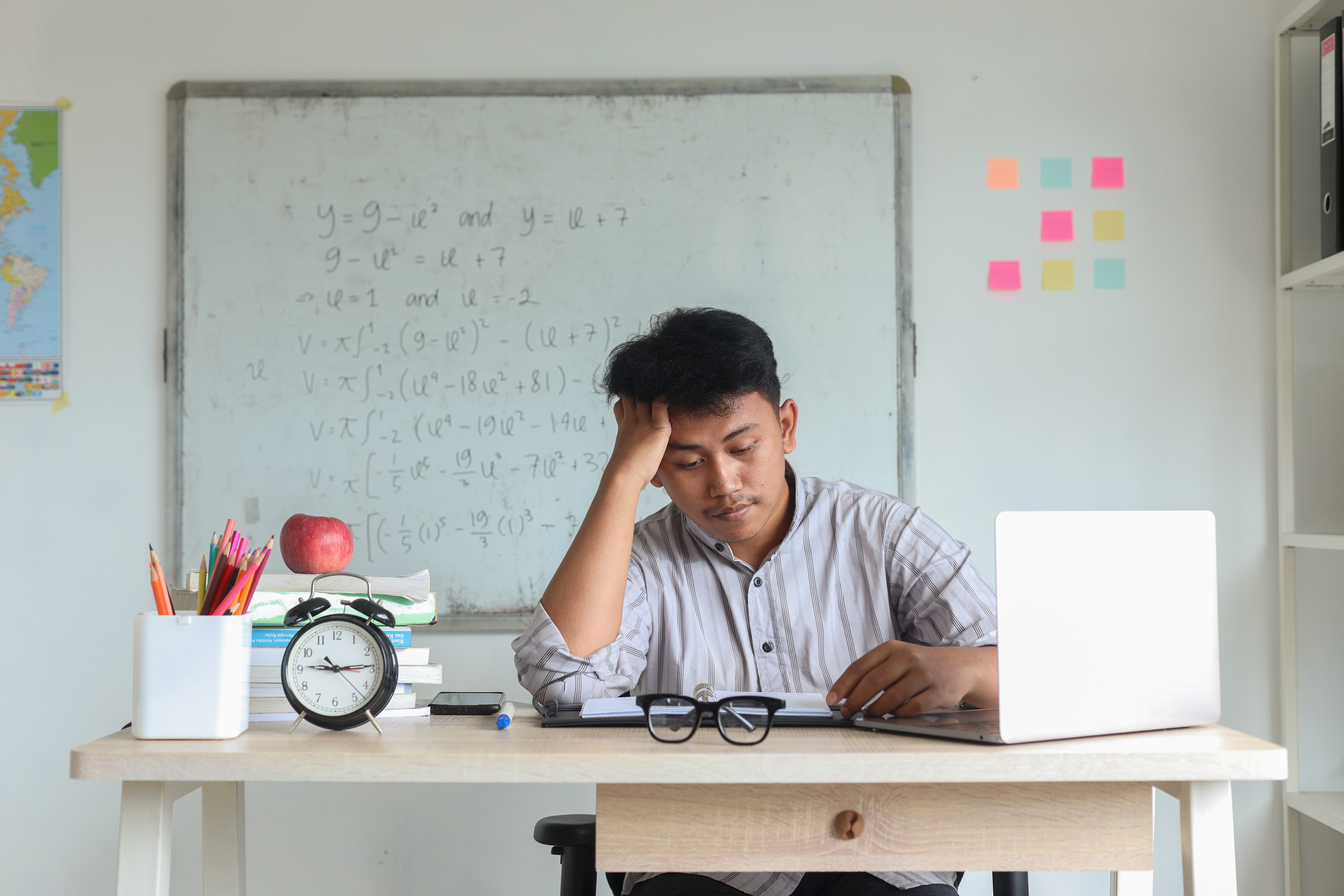 Stressed teacher sitting in front of a white board with comlex mathematical equations on it