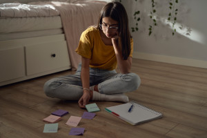 Teenage girl sitting on floor and trying to learn with post-it notes