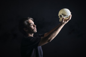 An actor, presumably playing Hamlet, holding up a skull while standing on an all-black stage