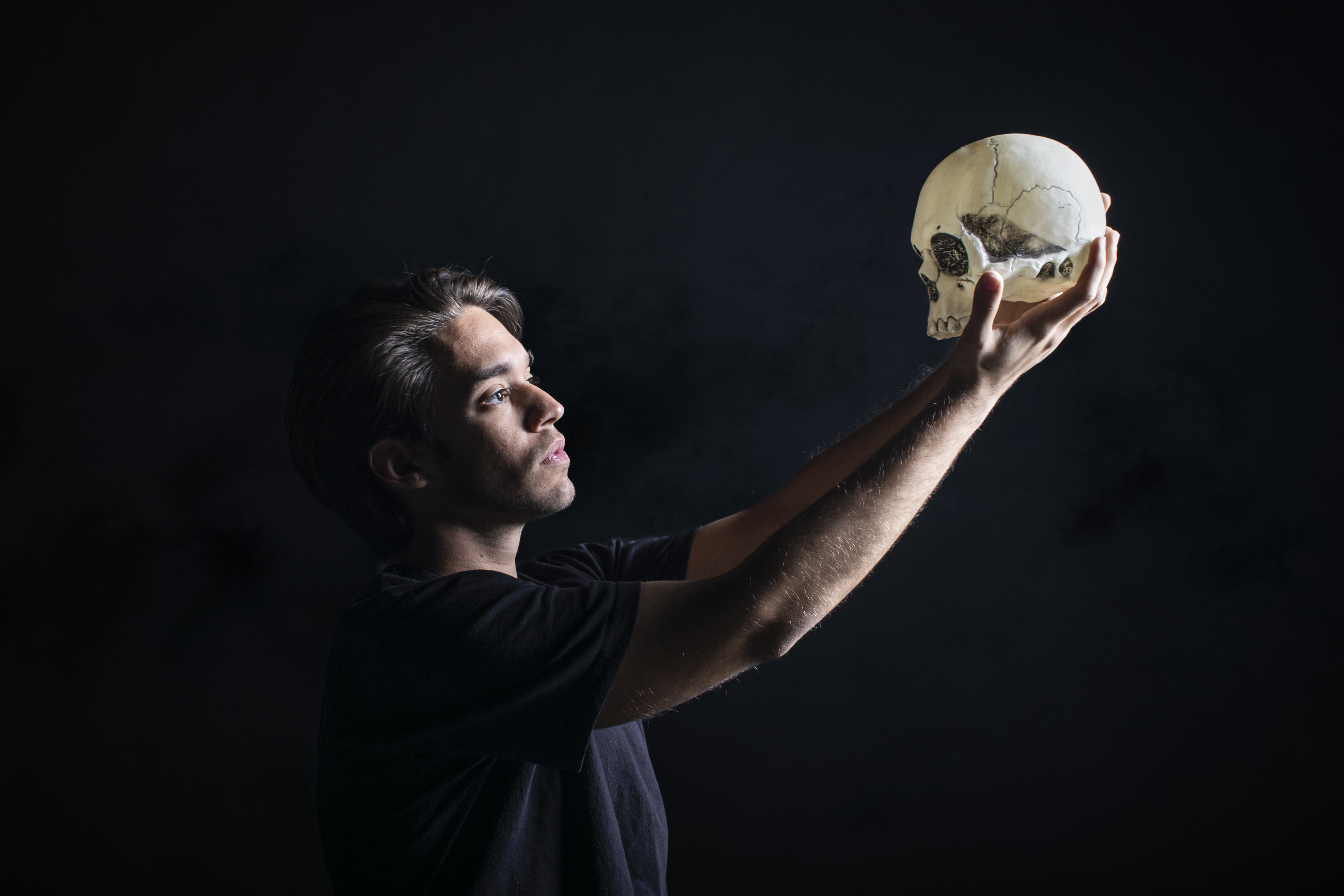 An actor, presumably playing Hamlet, holding up a skull while standing against an all-black background