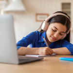 Middle schooler wearing headphones and doing work in front of her laptop at a desk