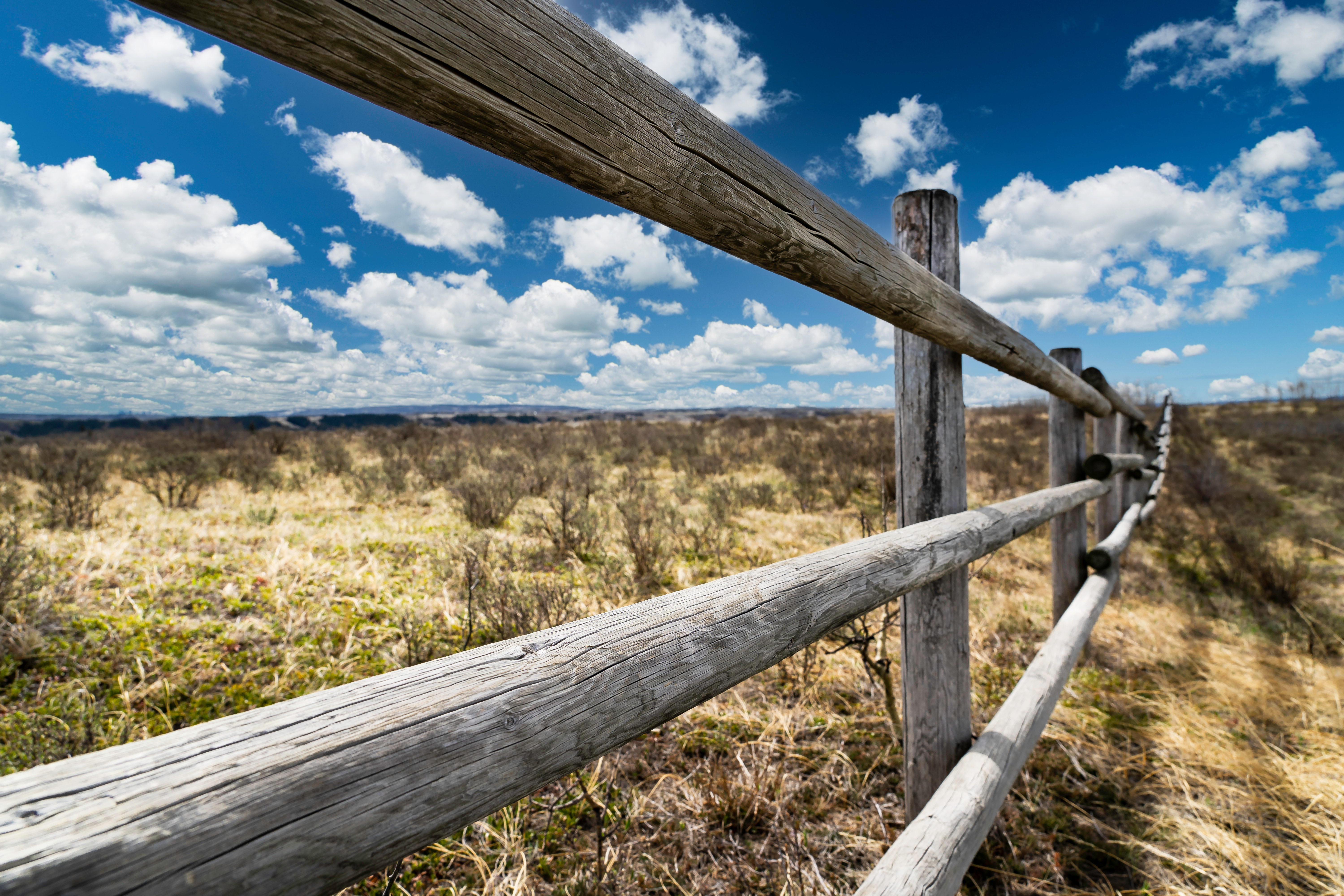 A closeup view looking along a post-an-rail fence on a prairie of brown and green