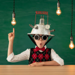 A happy student wearing a vest, bow tie, and an upside-down colander on his head, holding a finger up in the air as lightbulbs glow around him