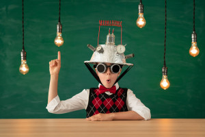 A happy student wearing a vest, bow tie, and an upside-down colander on his head, holding a finger up in the air as lightbulbs glow around him