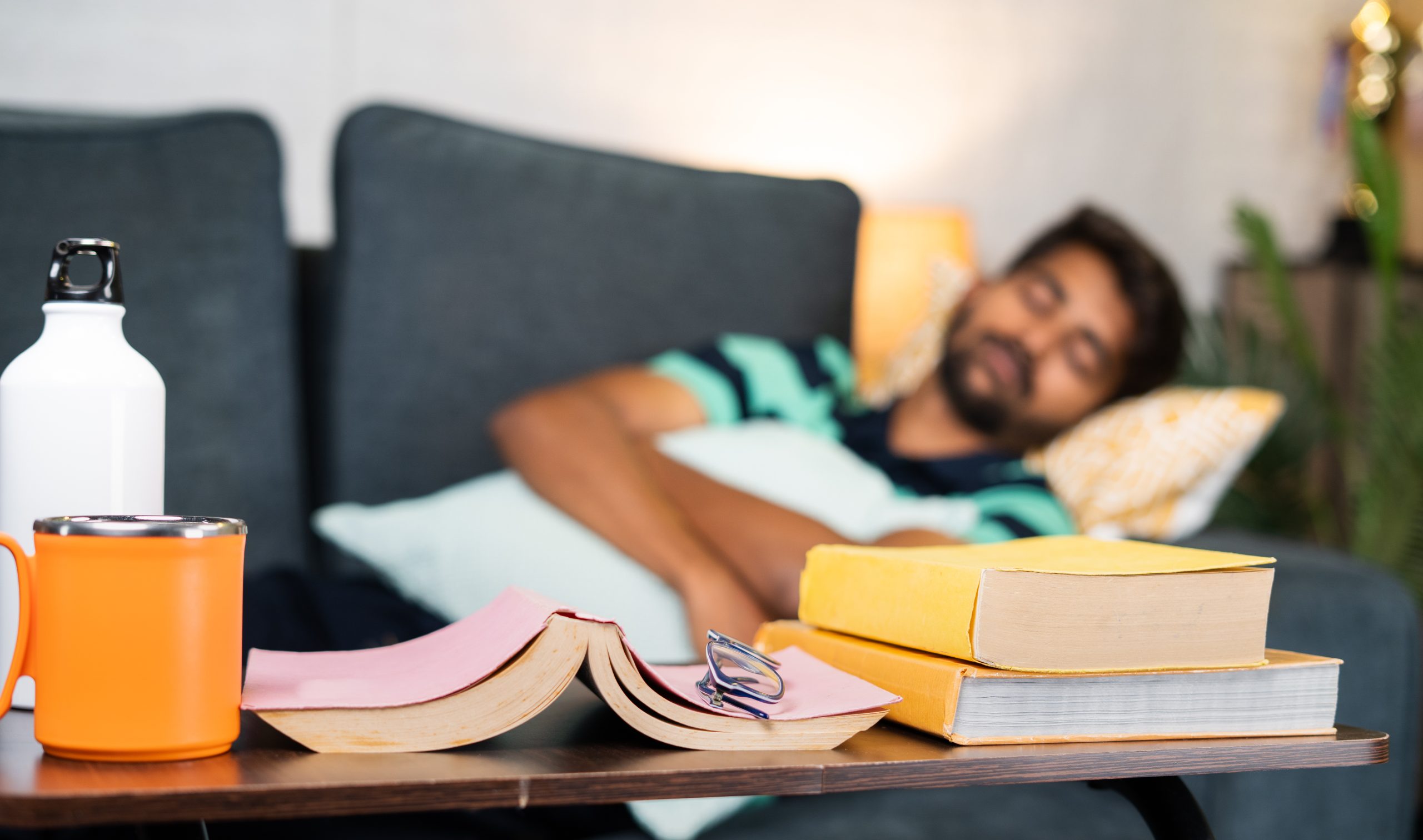 Young man sleeping on sofa infront of book while studying for examination at home